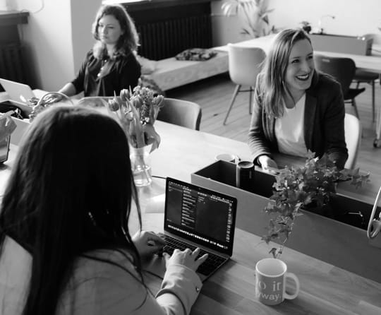 smiling women sitting at desks and working on laptops