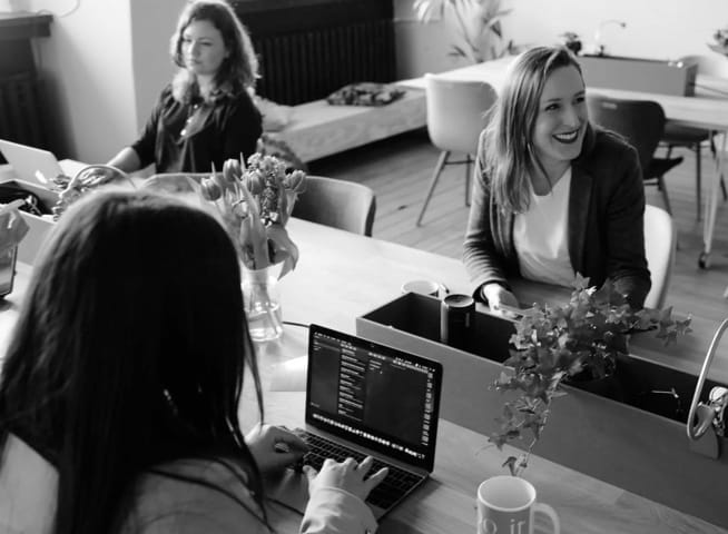 smiling women sitting at desks and working on laptops